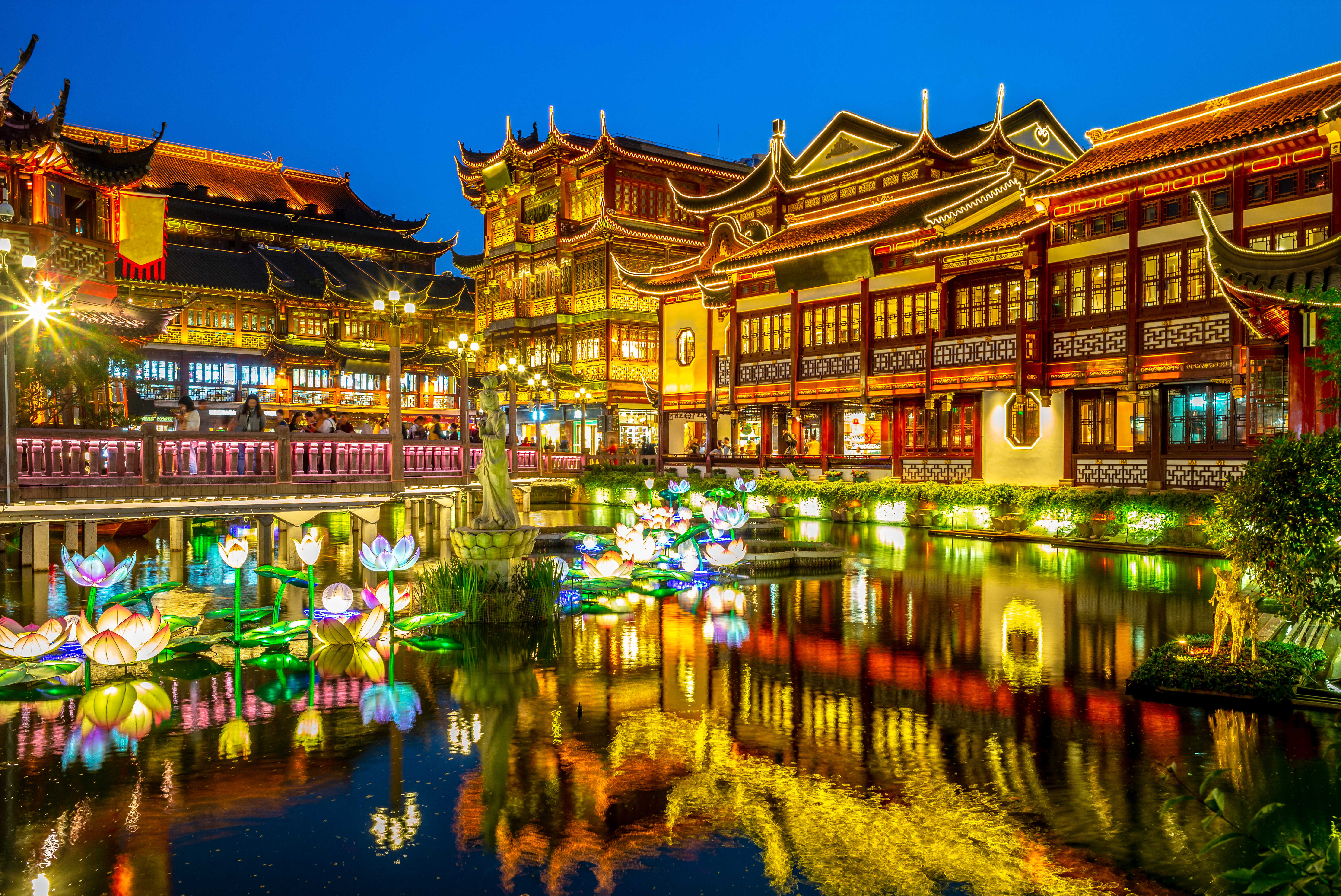 Yu Garden in Shanghai lit up at night, with illuminated lotus lanterns floating on the pond before traditional pavilions