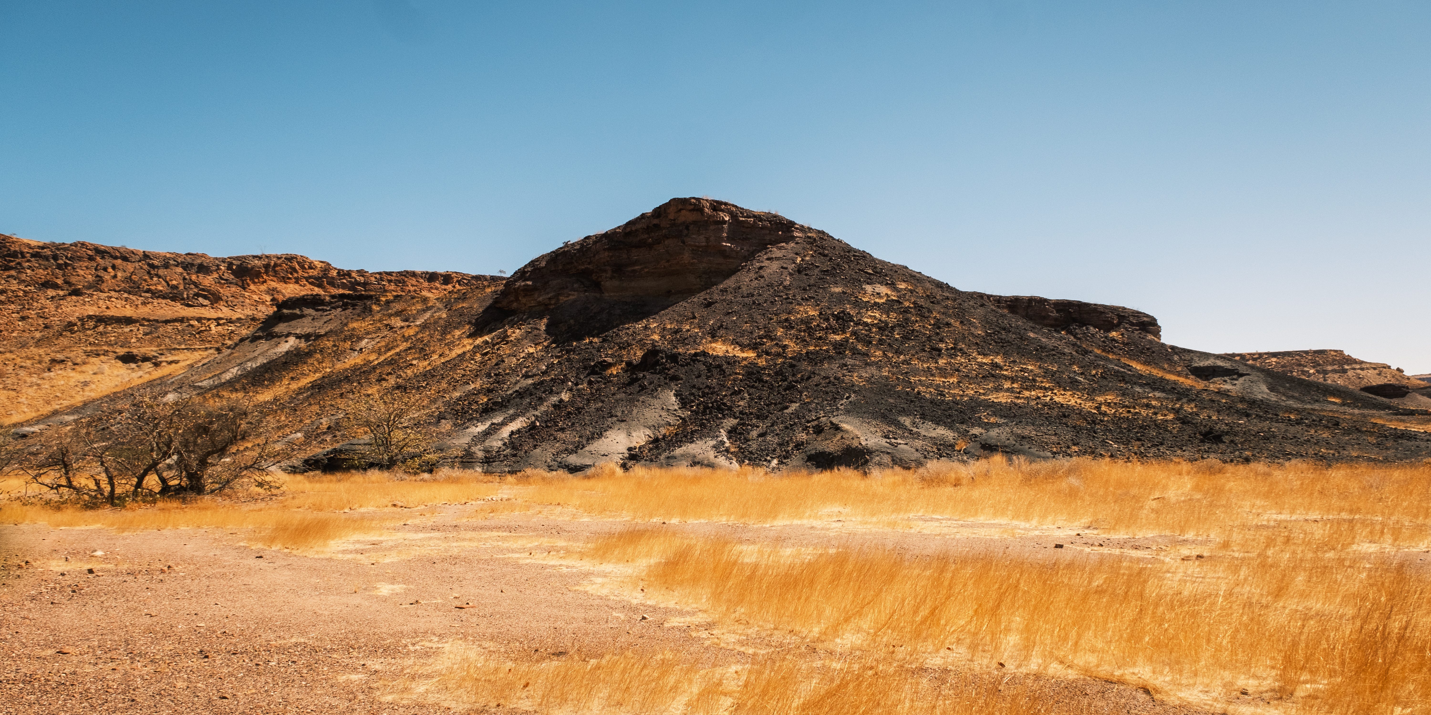 Dark solidified lava flow forming a rounded hill at Burnt Mountain, with dry golden grass in the foreground, Namibia