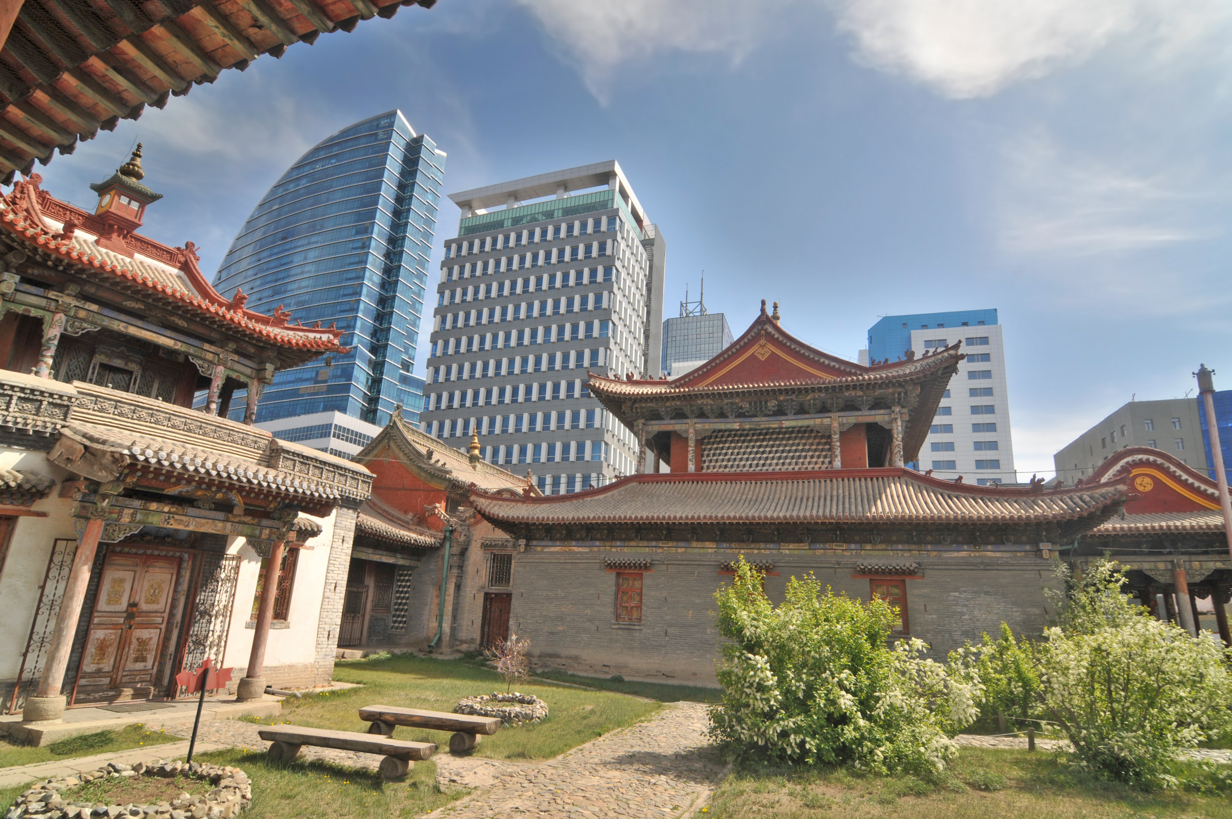 Red and gold temple roofs of the Choijin Lama Temple monastery courtyard in Ulaanbaatar, with glass skyscrapers rising behind