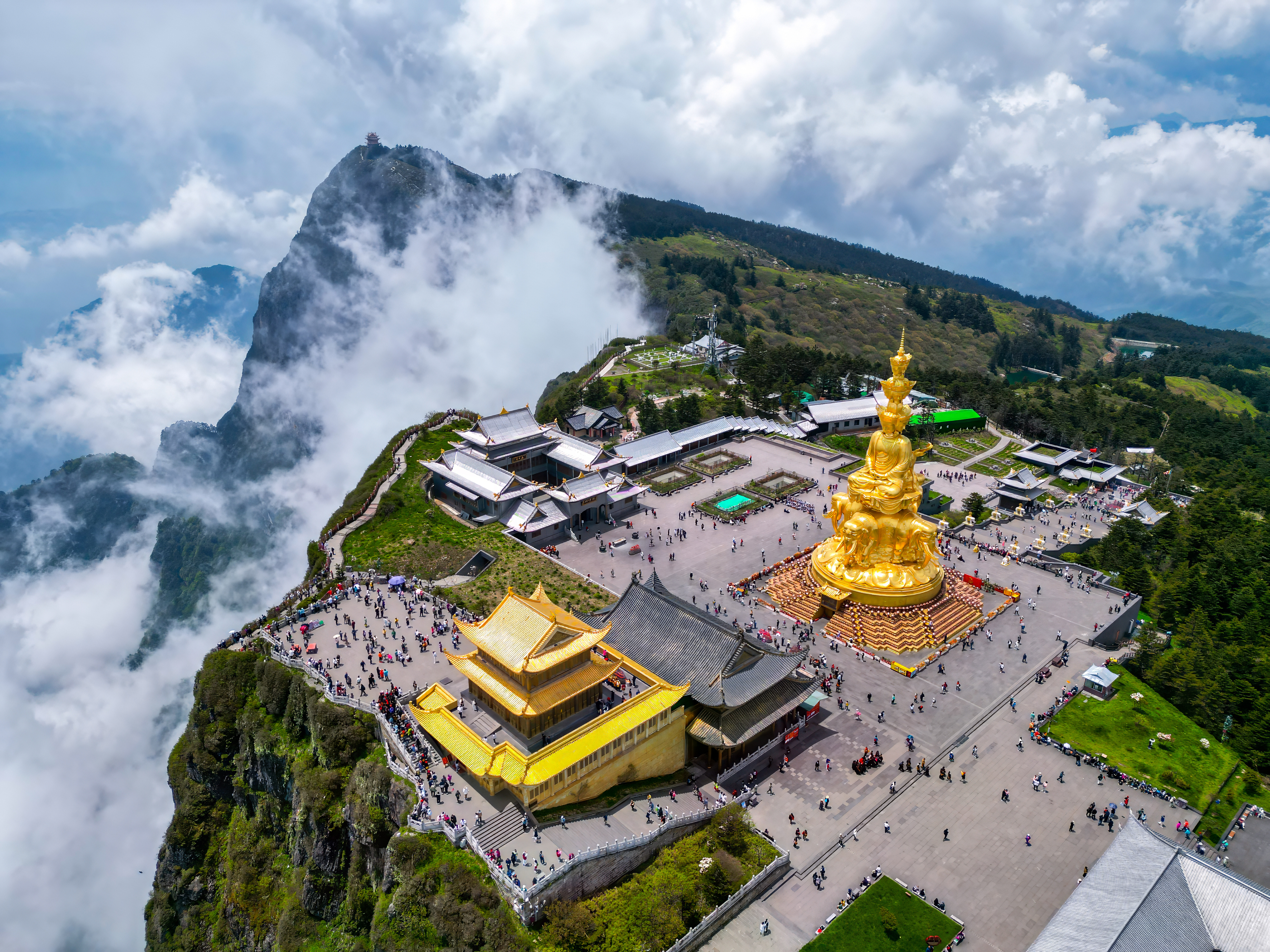 Aerial view of the Golden Summit of Mount Emei with its golden statue and temple buildings rising above clouds and forested ridges