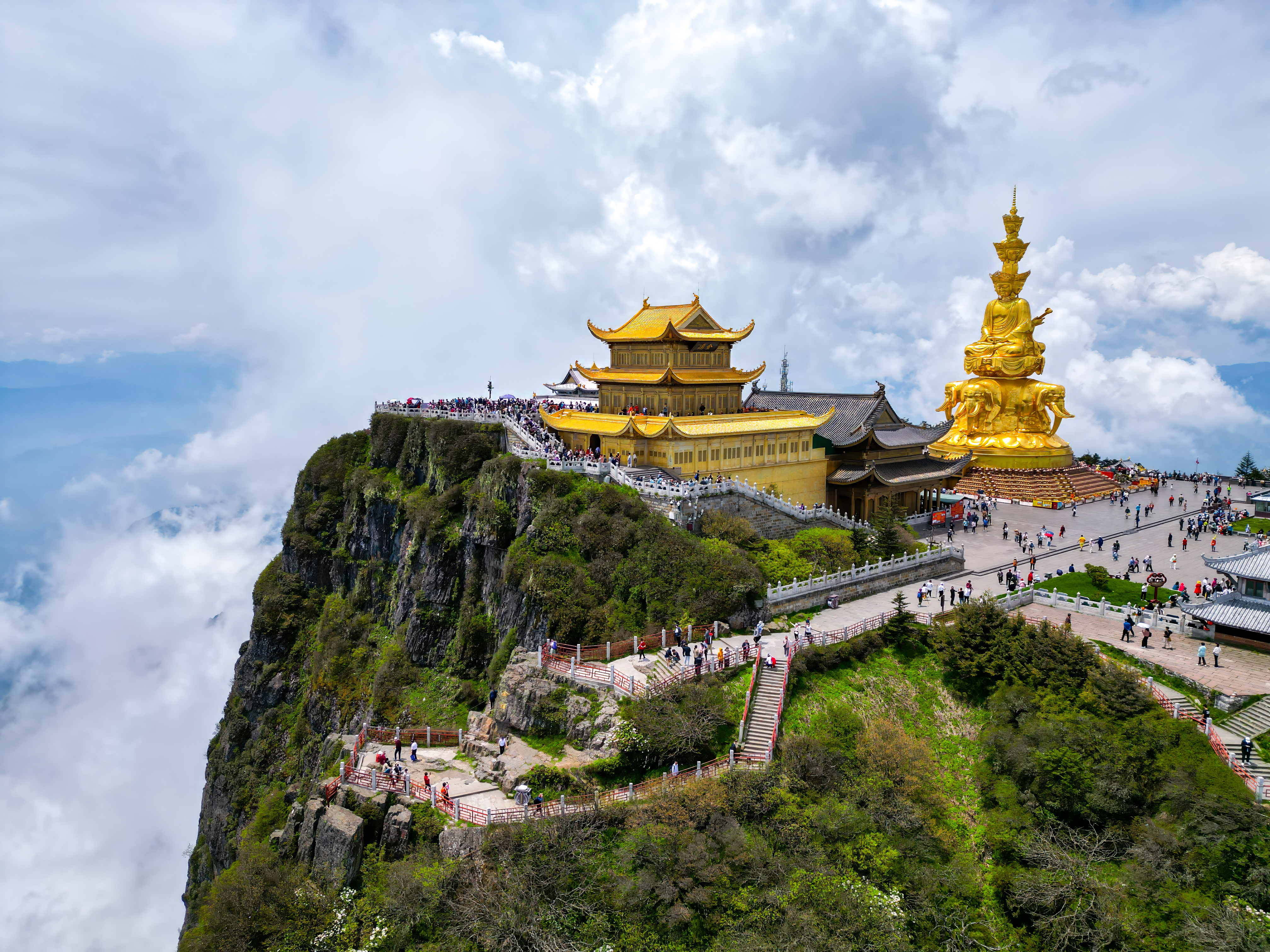 Aerial view of the Golden Summit of Mount Emei, a gilded temple and towering bodhisattva statue atop a cliff above clouds