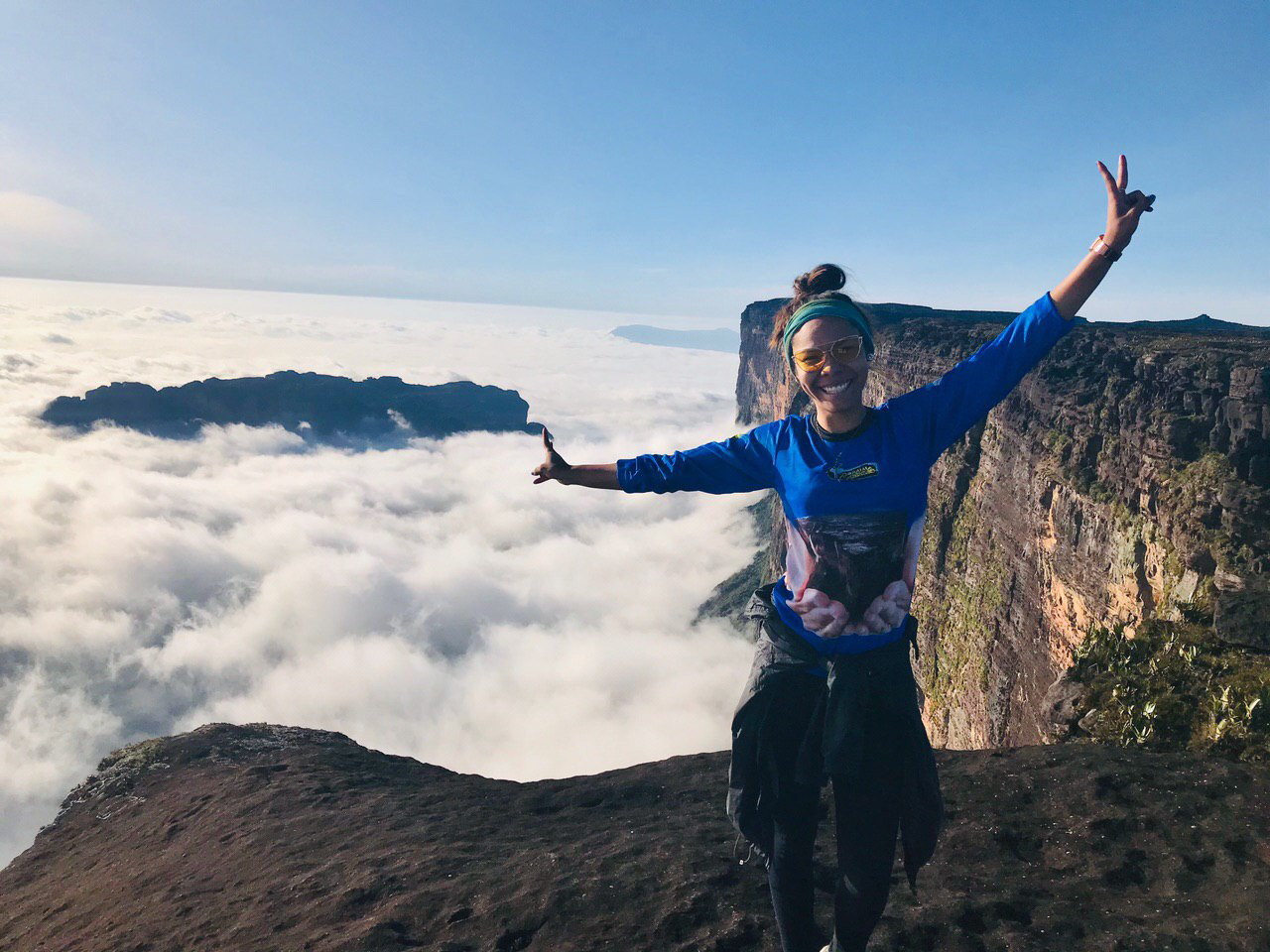 Hiker celebrates with raised arms atop Mount Roraima, Venezuela, overlooking a sea of clouds and neighboring tepui cliffs