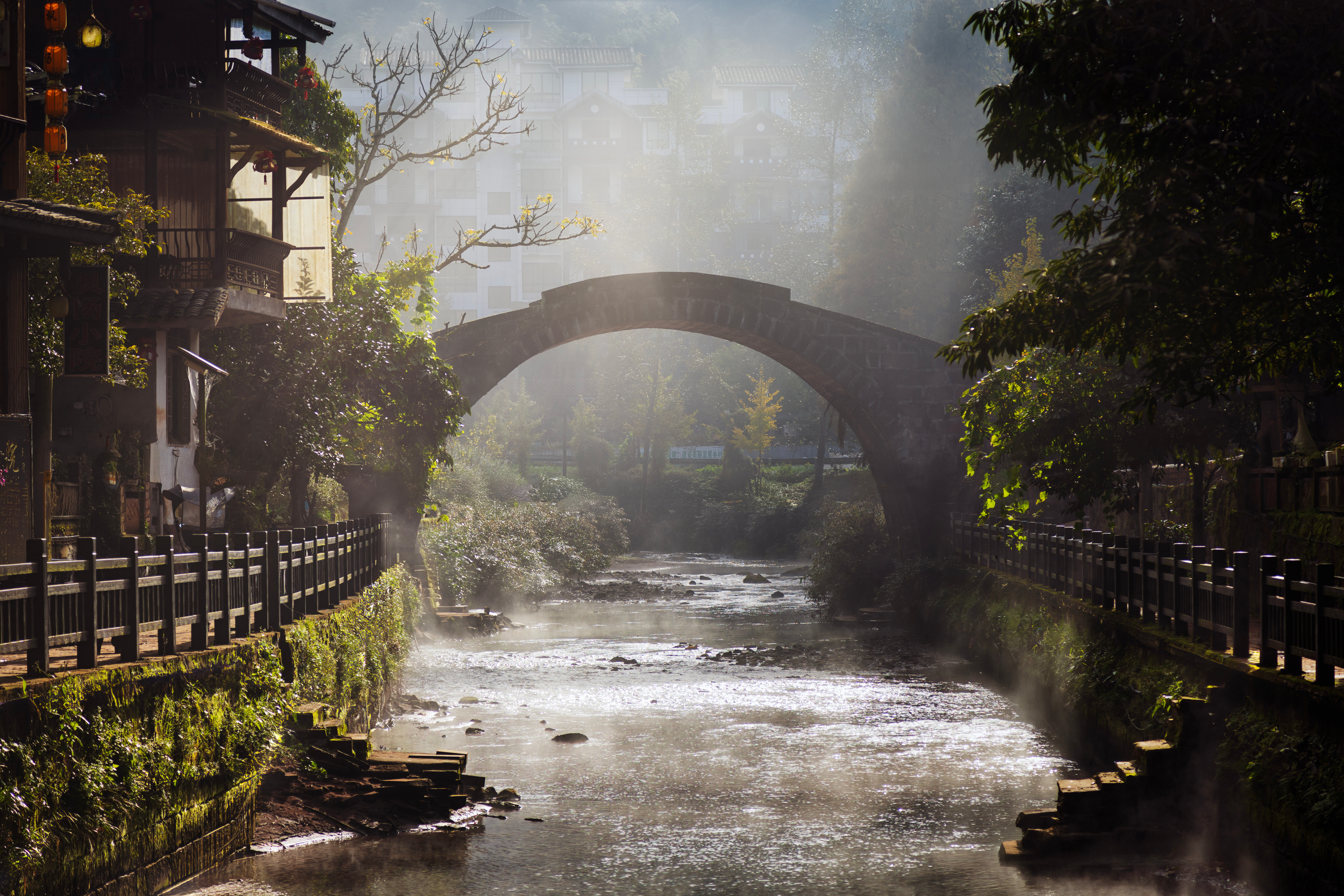 Stone arched bridge over a misty river in Shangli, lined with old wooden houses and stone-railed walkways