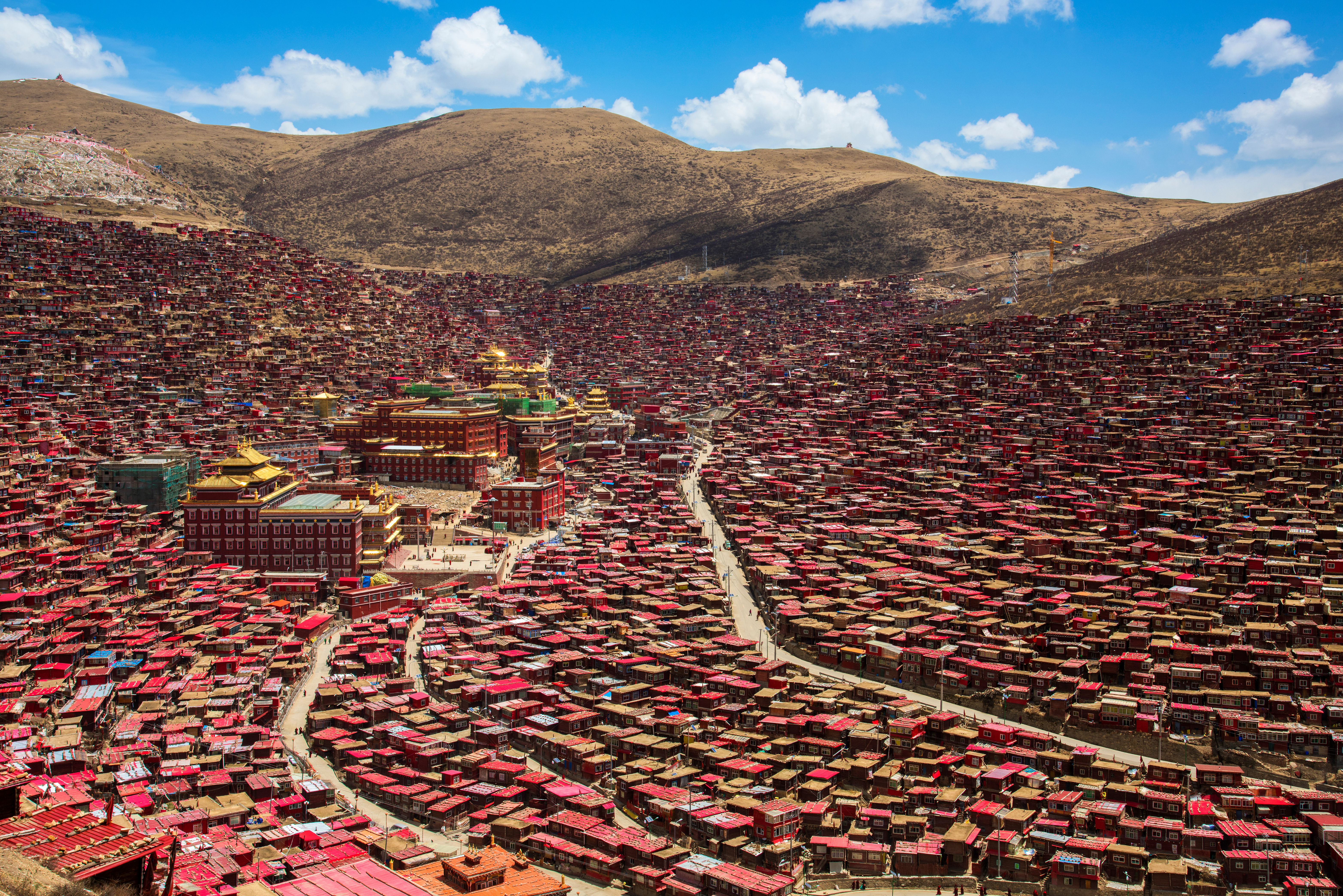 Thousands of densely packed red wooden dwellings fill a valley at Larung Gar in Sêrtar County, Sichuan, with golden-roofed temples at center
