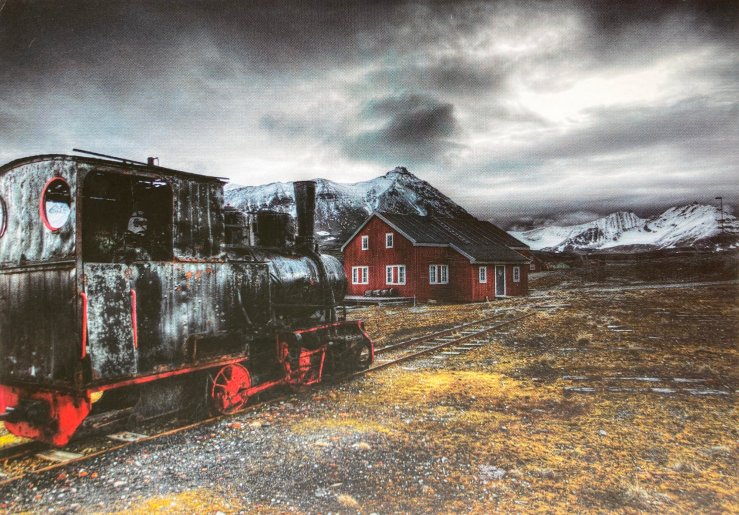 Image of a derelict train engine and a barn-red station building, in a stark and hostile-looking Arctic landscape.