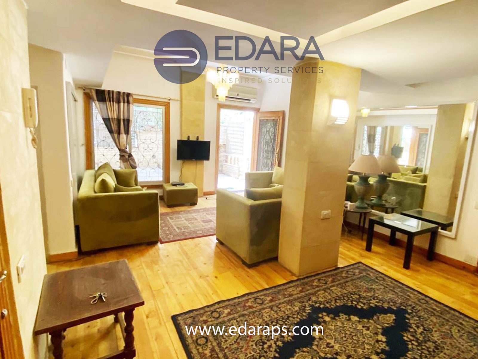 Living room area with green sofas, wooden flooring, and decorative mirrors in a residential space.
