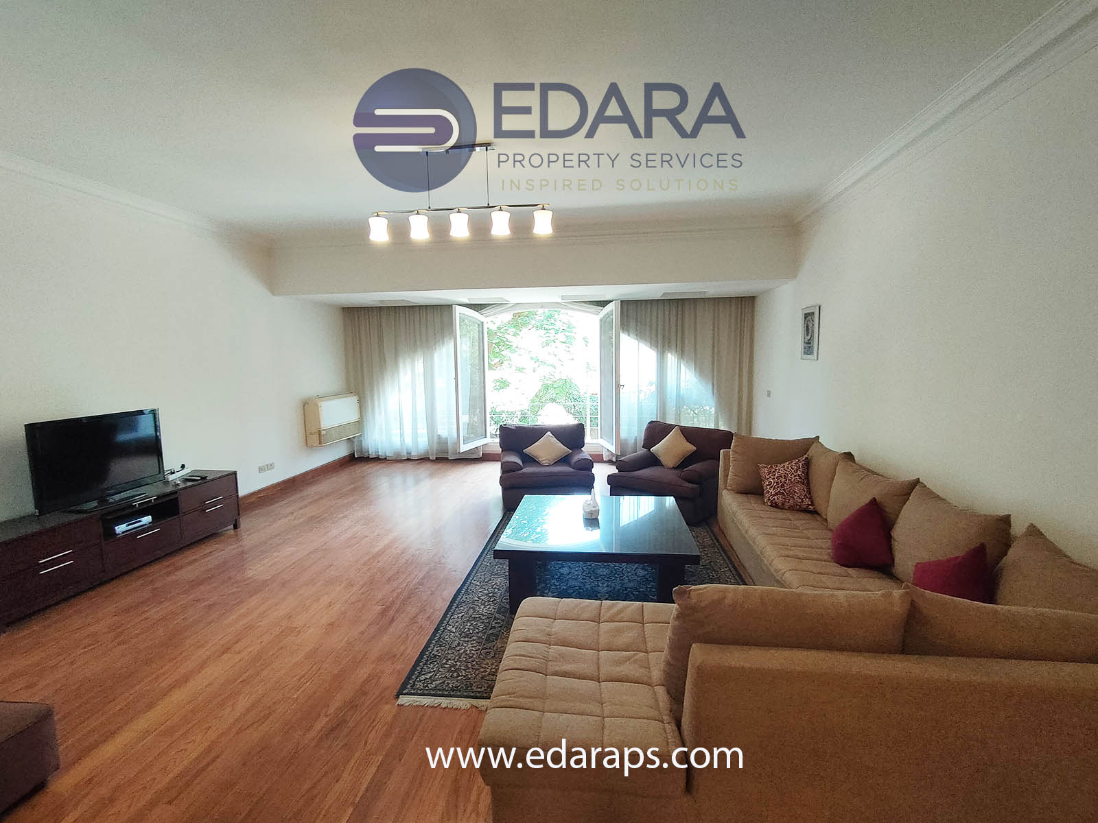 Living room featuring a large sofa set, a coffee table, and a television against a light-colored wall.