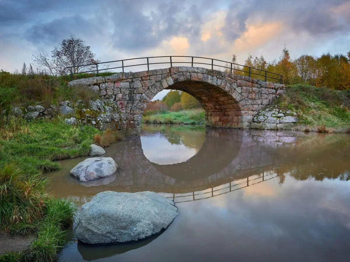 ld stone bridge reflecting over calm river at sunset, symbolizing connection and alignment between two sides