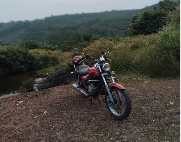 A red motorcycle parked in the dirt, surrounded by mountains.