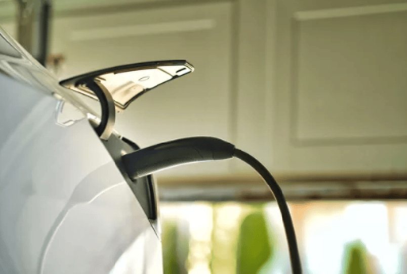 Electric vehicle charging cable plugged into a white car's charging port