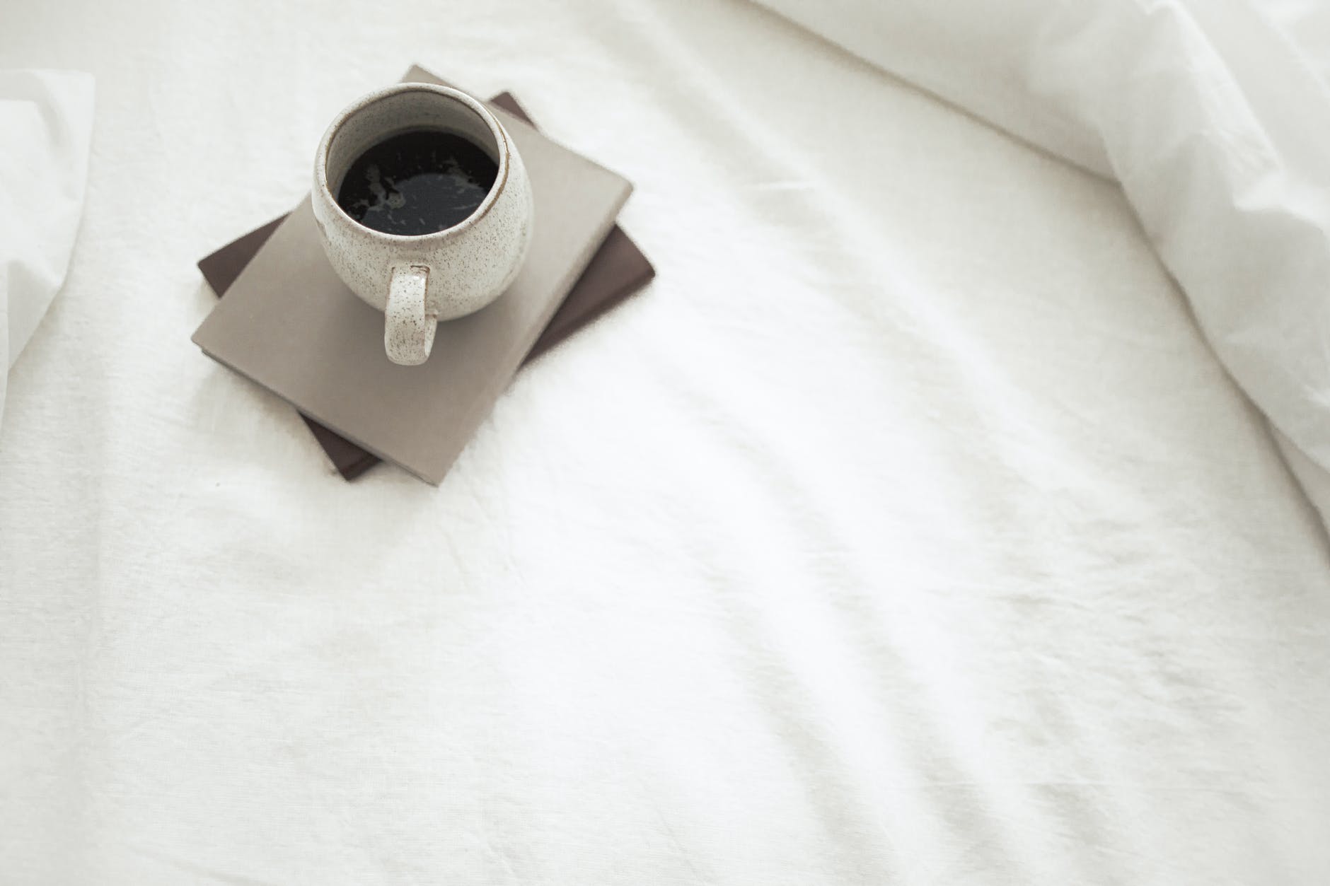 cup of aromatic coffee and notebooks placed on white bed