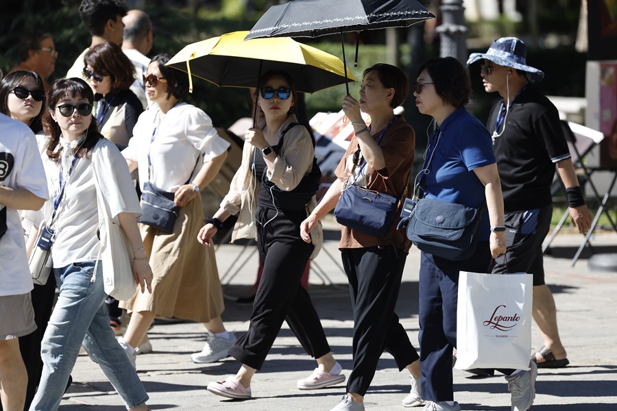 Un grupo de turistas se protege del sol con sombrillas en las inmediaciones del Museo del Prado