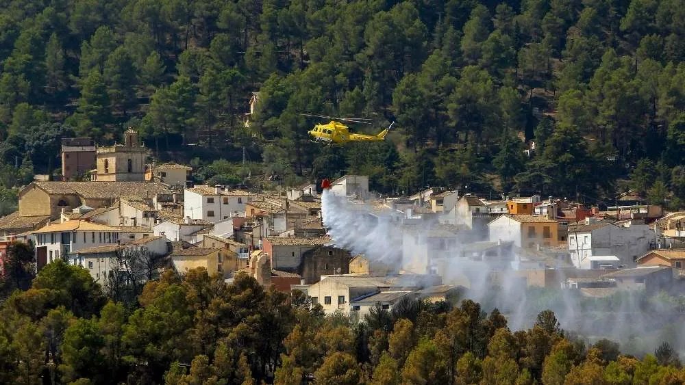 Un helicóptero trabaja refrescando el perímetro de la localidad alicantina de Penáguila para protegerla del incendio de su vecina Benasau.