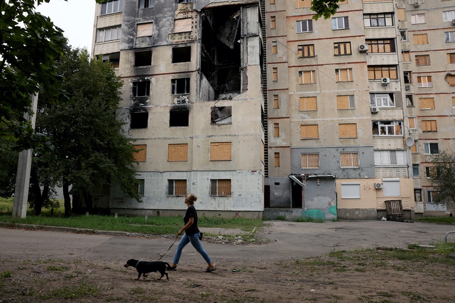 Una mujer pasea a su perro junto a un edificio dañado por los bombardeos en el distrito de Saltivka Norte de Kharkiv, Ucrania.