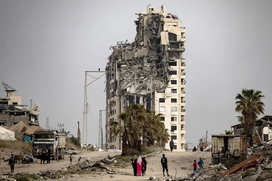 Palestinos desplazados internos caminan junto a edificios destruidos en el oeste de la Ciudad de Gaza