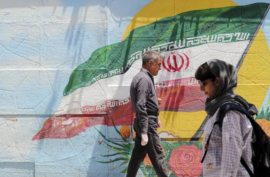 iraníes caminan junto a una pintura mural de la bandera nacional de Irán en Teherán, Irán