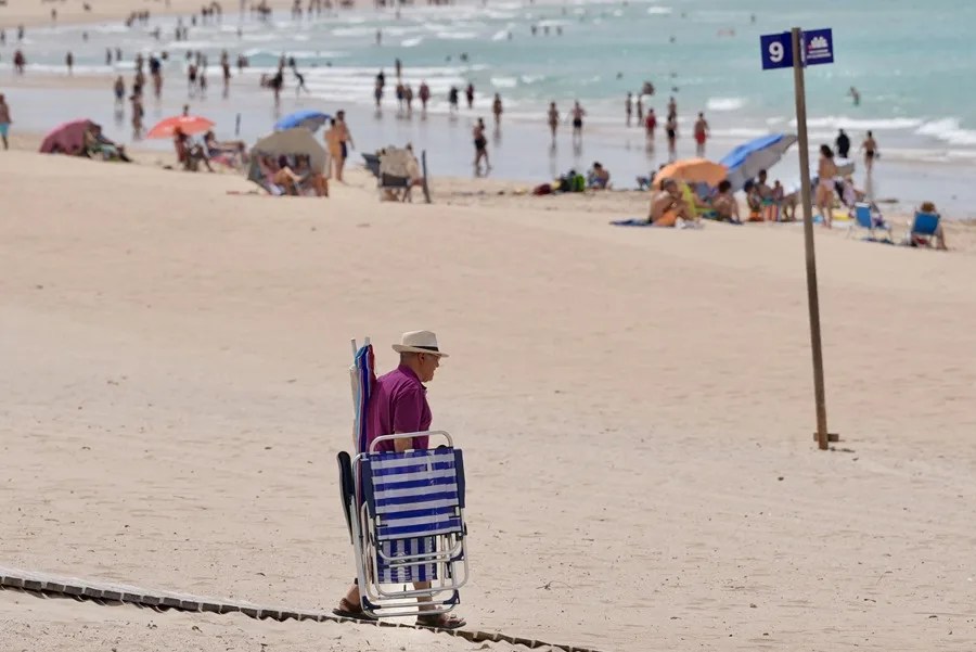 Un hombre cargado con sillas y sombrillas camina por la playa de Chiclana de la Frontera (Cádiz).