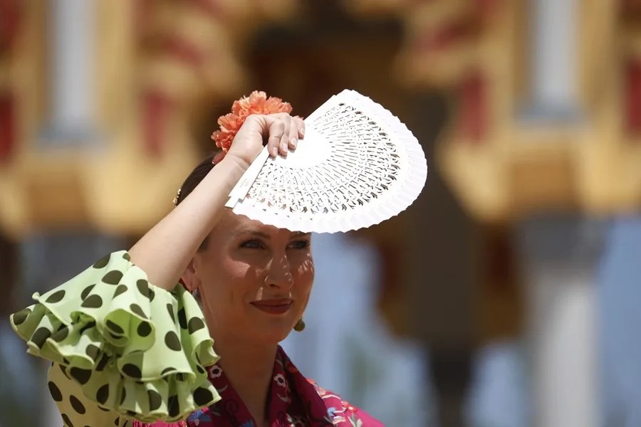 Una mujer vestida de flamenca se cubre los ojos con un abanico en Córdoba.