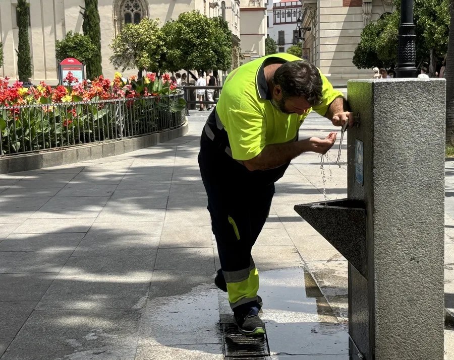 Un operario bebe agua de una fuente del centro de Sevilla