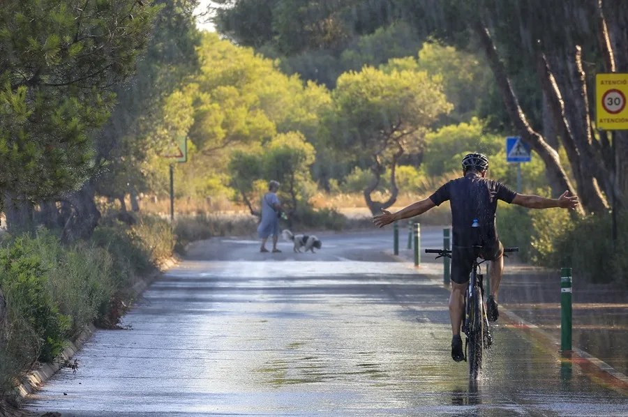 Un ciclista se refresca bajo el funcionamiento de los cañones de agua activados este miércoles por el Ayuntamiento de Valencia.