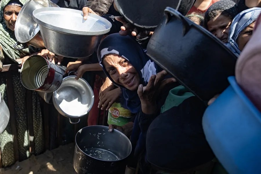 Palestinos hacen cola para recibir comida de una cocina que proporciona alimentos gratuitos a desplazados en Khan Yunis