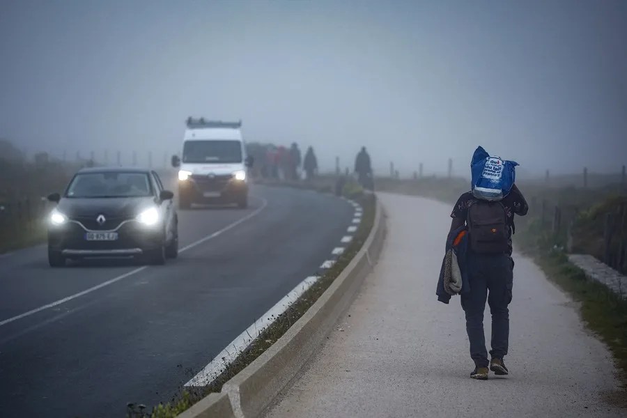 Migrantes caminan por la carretera a primera hora de la mañana tras intentar cruzar el Canal de la Mancha a las afueras de Wimereux