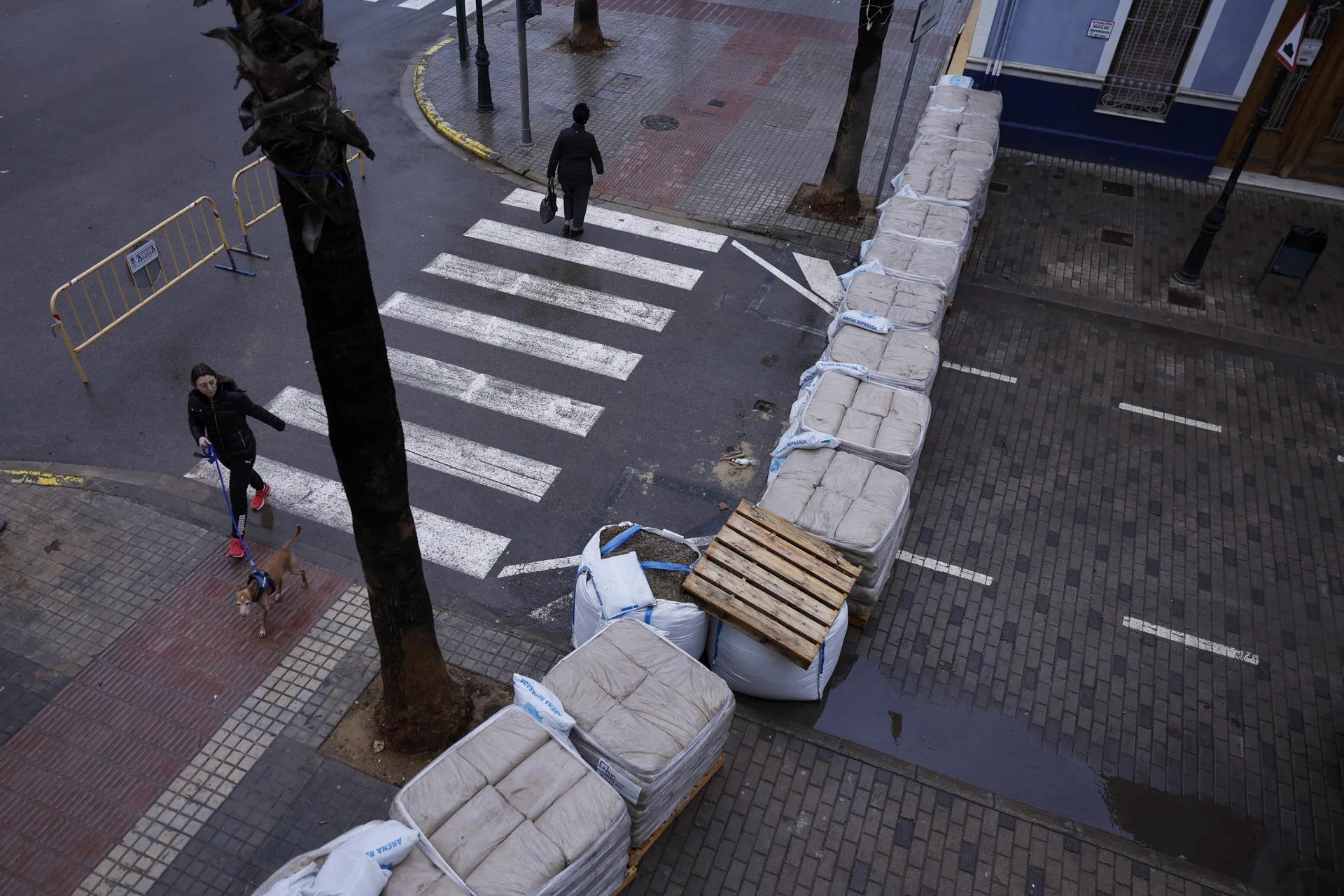 Dos personas pasan junto a un improvisado dique levantado con sacos de arena en las calles colindantes a un barranco en Aldaia. EFE/Kai Försterling
