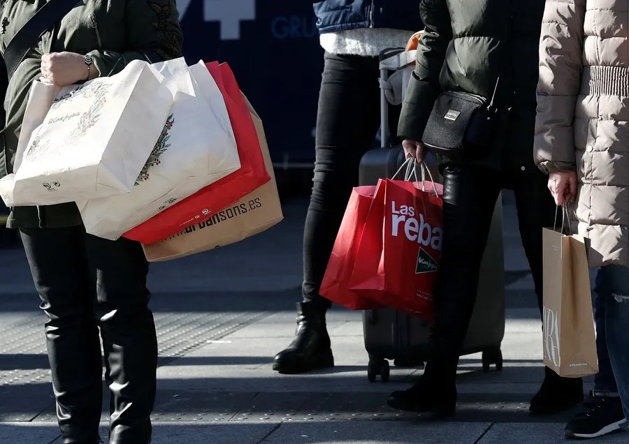Un grupo de personas esperan en un paso de cebra con varias bolsas