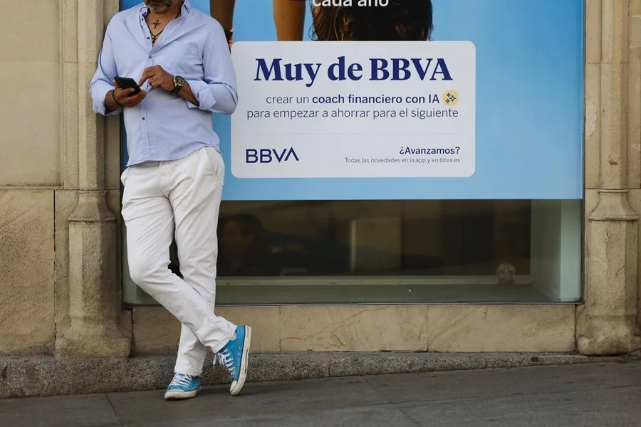 Un viandante revisa su teléfono junto a una sucursal del banco BBVA