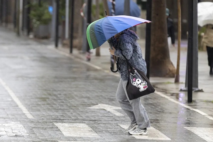 Una persona se resguarda con un paraguas de la lluvia y el viento este jueves en Huelva