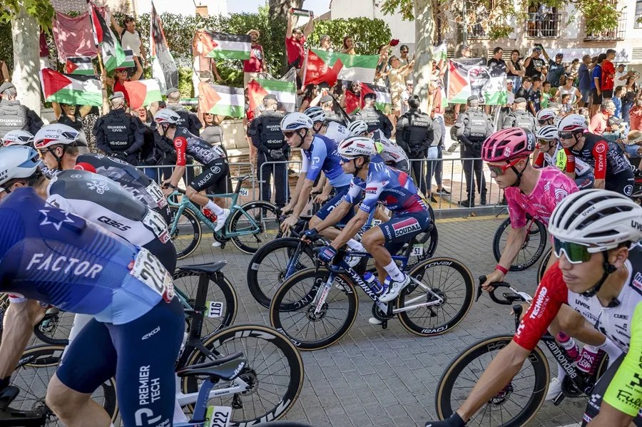 Los corredores del equipo Israel Premier Tech pasan delante de la manifestación propalestina