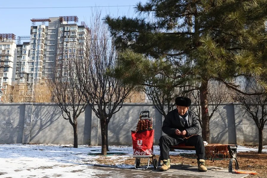 Un anciano se sienta junto a edificios residenciales en Pekín