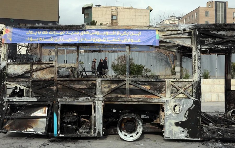 Iraníes caminan junto a los restos de un autobús público incendiado en Teherán, Irán, este jueves.