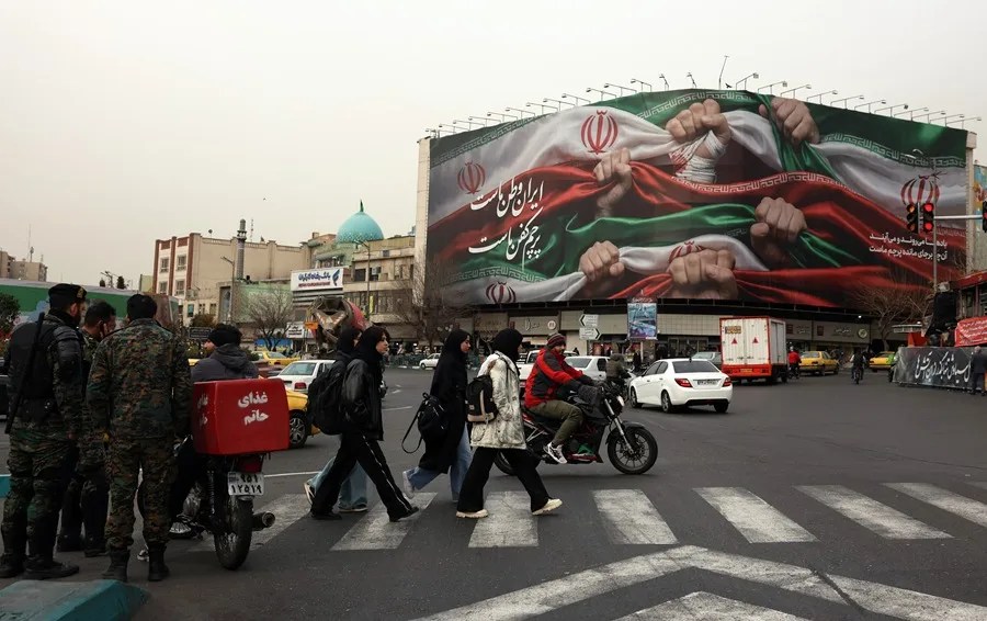 Iraníes caminan junto a una valla publicitaria en persa que dice "Irán es nuestra patria" en una calle de Teherán