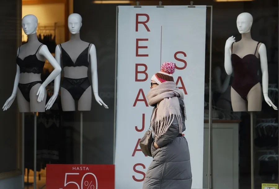 Una viandante, bien abrigada para hacer frente al frío invernal de Pamplona, pasa frente a un escaparate que anuncia el inicio de las rebajas