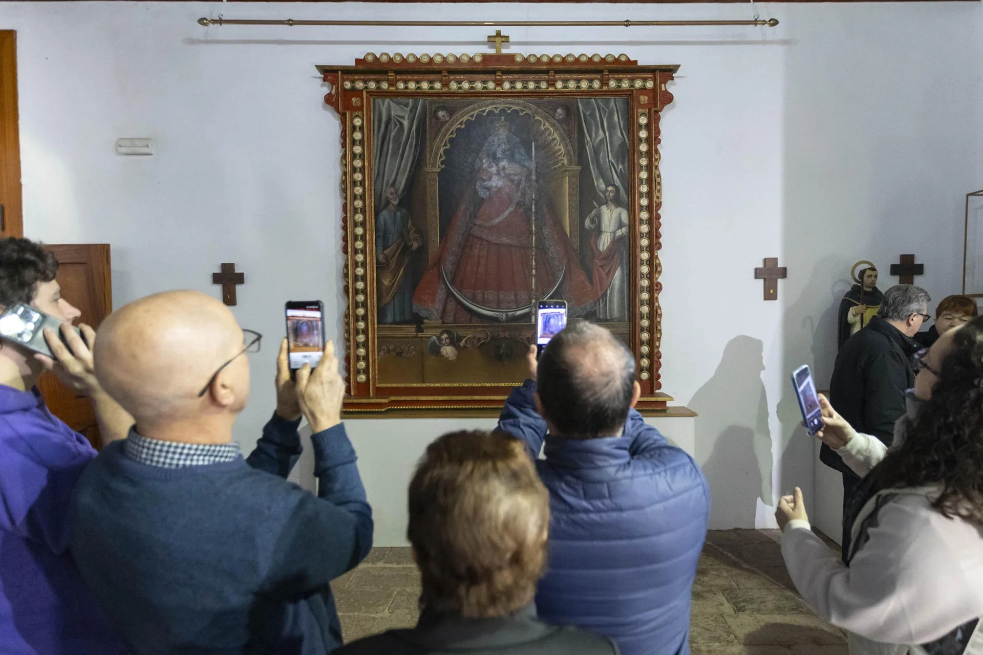 Vecinos de Taganana fotografían con sus móviles la imagen de la Virgen de Candelaria, cuyo retablo fue presentado este sábado una vez finalizado el proceso de restauración. EFE/ Miguel Barreto