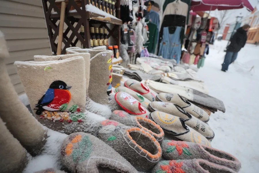 Una mujer camina frente a una tienda callejera que vende valenki (botas de fieltro tradicionales rusas