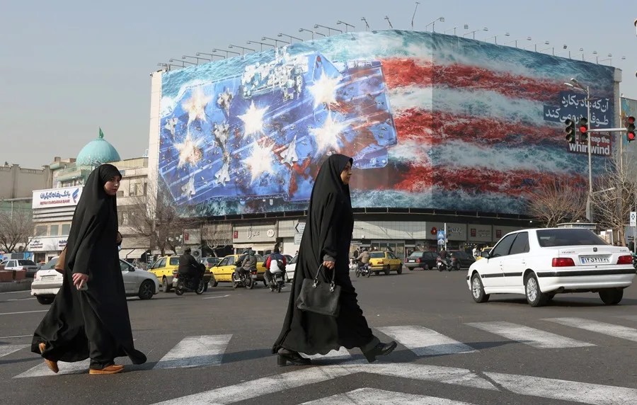 Mujeres iraníes caminan cerca de un valla publicitaria antiestadounidense instalada en la plaza Enqelab, en Teherán