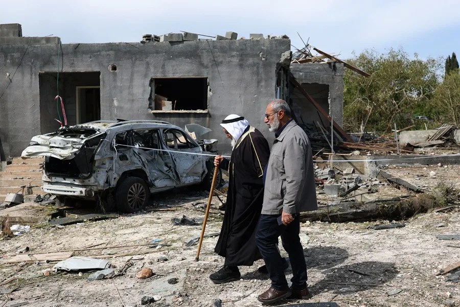 Un grupo de personas pasa junto a un edificio destruido en Zarzir, Israel