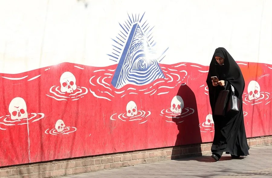 Una mujer iraní con velo camina junto a un mural antiestadounidense en Teherán