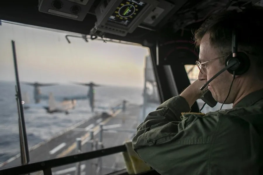 Un oficial naval a bordo del USS Tripoli (LHA 7) supervisa las operaciones de vuelo desde la torre de control mientras el buque de asalto anfibio navega en el mar Arábigo.