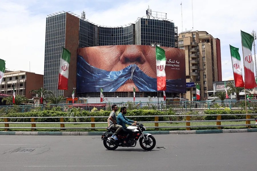 Varias personas en motocicleta se acercan a una enorme valla publicitaria antiestadounidense con una foto del presidente estadounidense, Donald Trump, en Teherán.