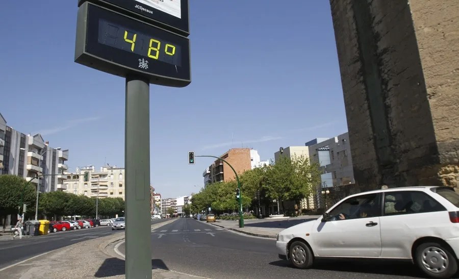 Un coche circula esta tarde, ante un termómetro que marca 48 grados