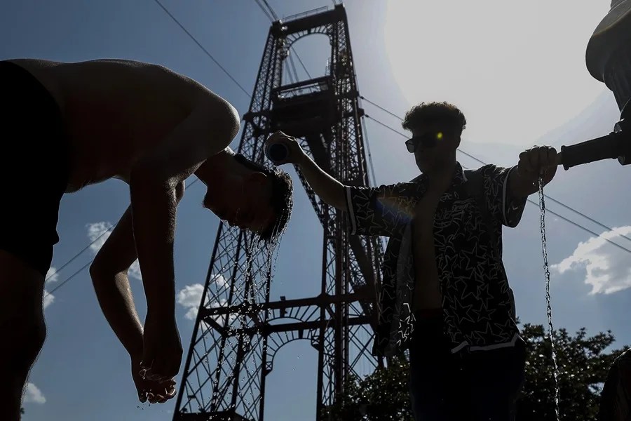 Dos jóvenes se refrescan en una fuente frente al Puente de Bizkaia en Getxo (Bizkaia)