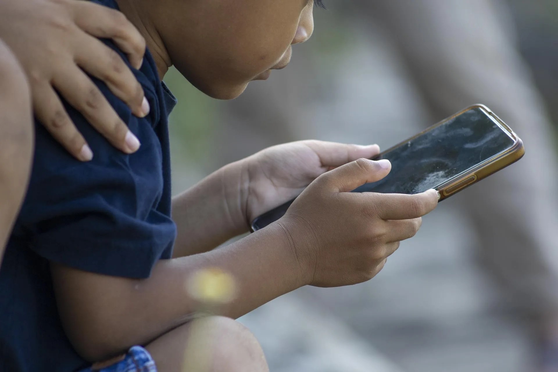 (FILE) A child uses a mobile phone at a park in Denpasar, Bali, Indonesia, 28 March 2026. EFE/EPA/MADE NAGI