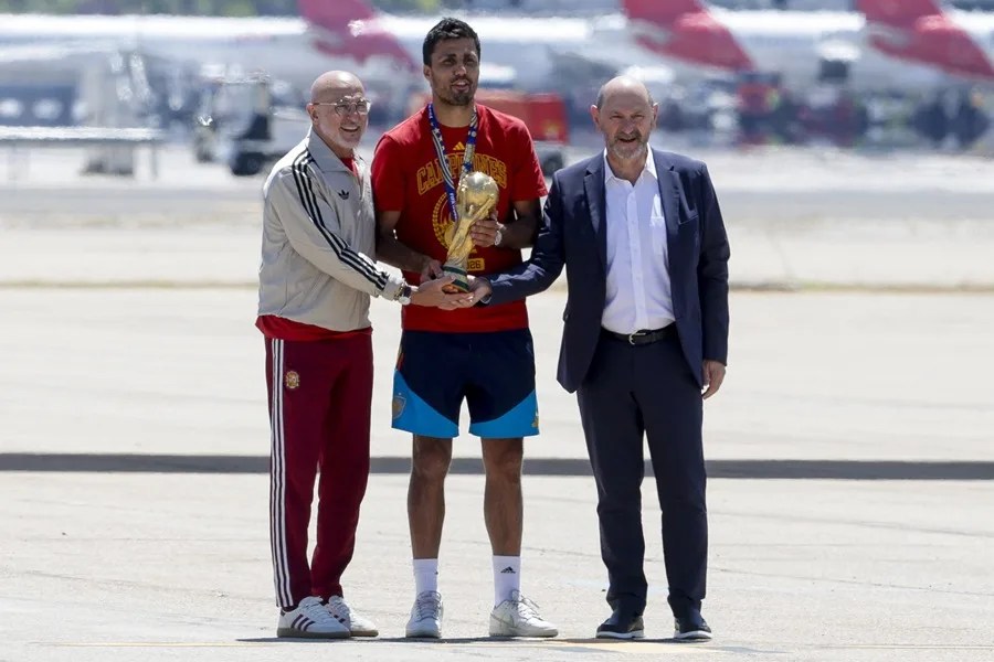 El capitán de la selección española de fútbol, Rodri (c), que lleva el  trofeo de la Copa del Mundo, acompañado del seleccionador nacional, Luis de la Fuente (i), a su llegada al aeropuerto de Madrid Barajas 