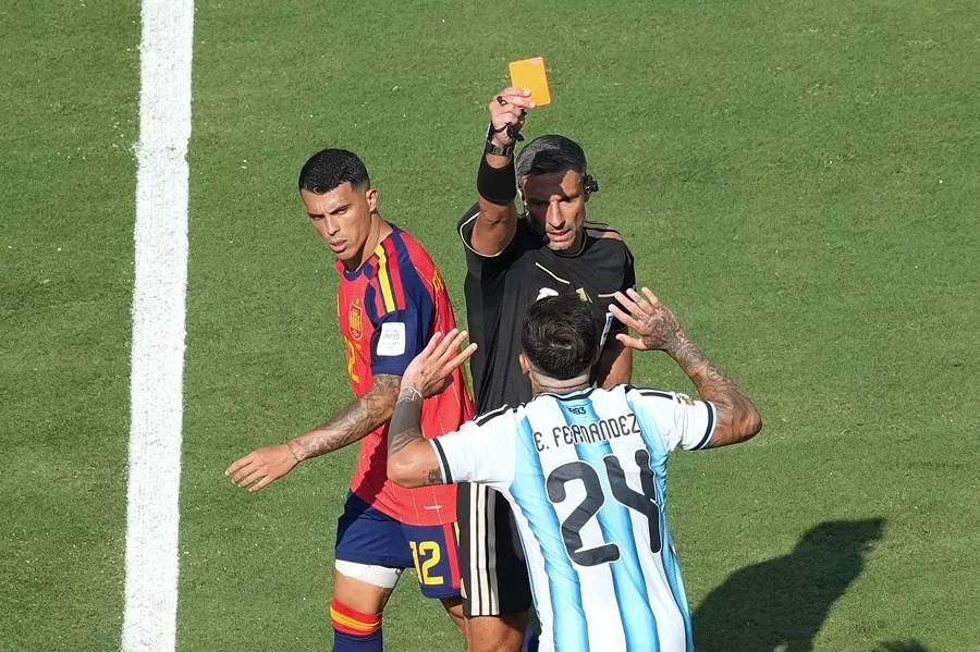 El árbitro esloveno Slavko Vincic (arriba, centro) muestra una tarjeta amarilla a Enzo Fernández (abajo, centro), de Argentina, durante la final de la Copa Mundial de la FIFA 2026