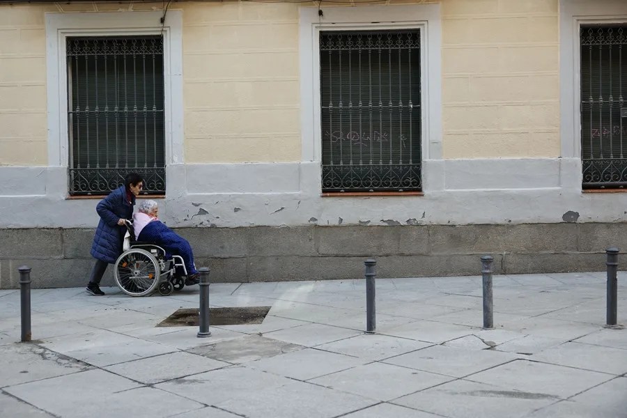 Una anciana en silla de ruedas y su cuidadora durante un paseo por Madrid.