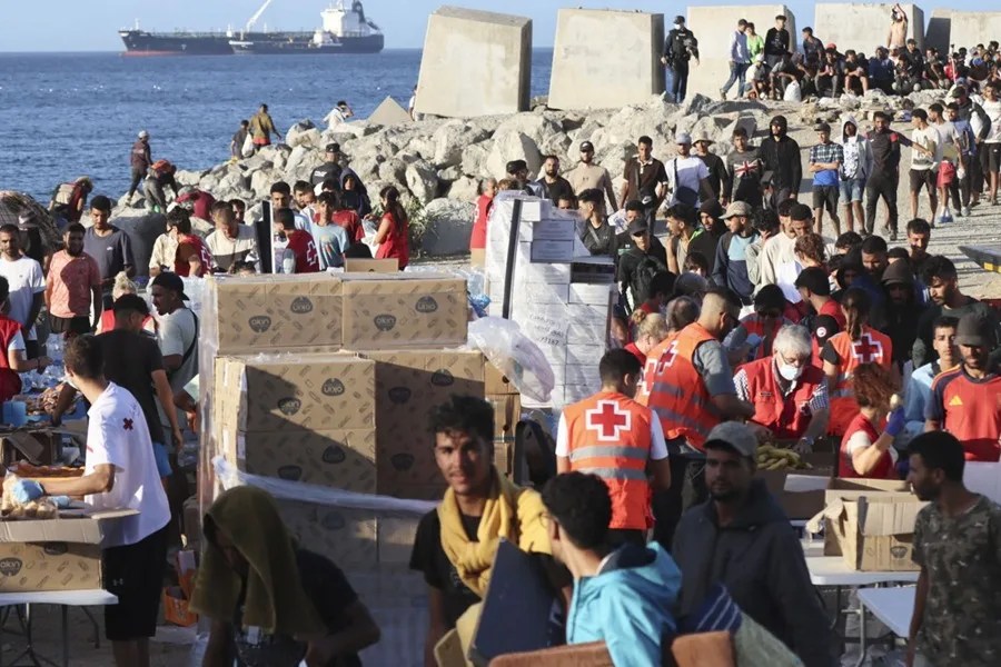 Inicio del reparto de alimentos por parte de miembros de Cruz Roja a los migrantes en la playa del Trampolín, este jueves en Ceuta.