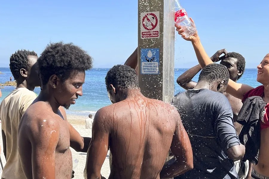 Jóvenes llegados a Ceuta se lavan en una ducha en la playa.